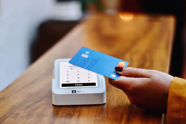 A hand paying a card machine via contactless with a blue bank card.