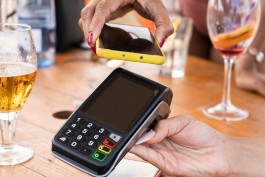 A portable card reader machine taking a payment at a pub table. There are half empty glasses in the background of where the payment is taking place.